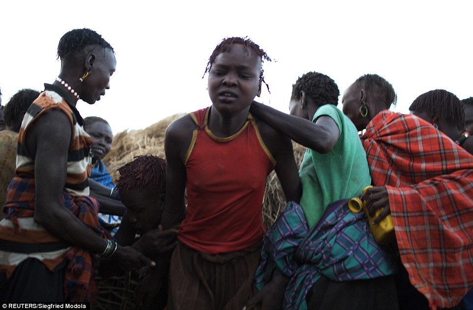 Village elders push a young girl out of a hut to take her to the place where her circumcision will be performed