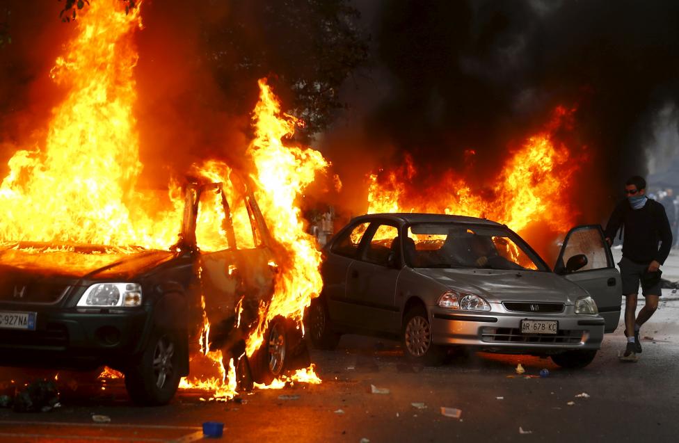 A man is helped to save his car set on fire by protesters during a rally against Expo 2015 in Milan, Italy