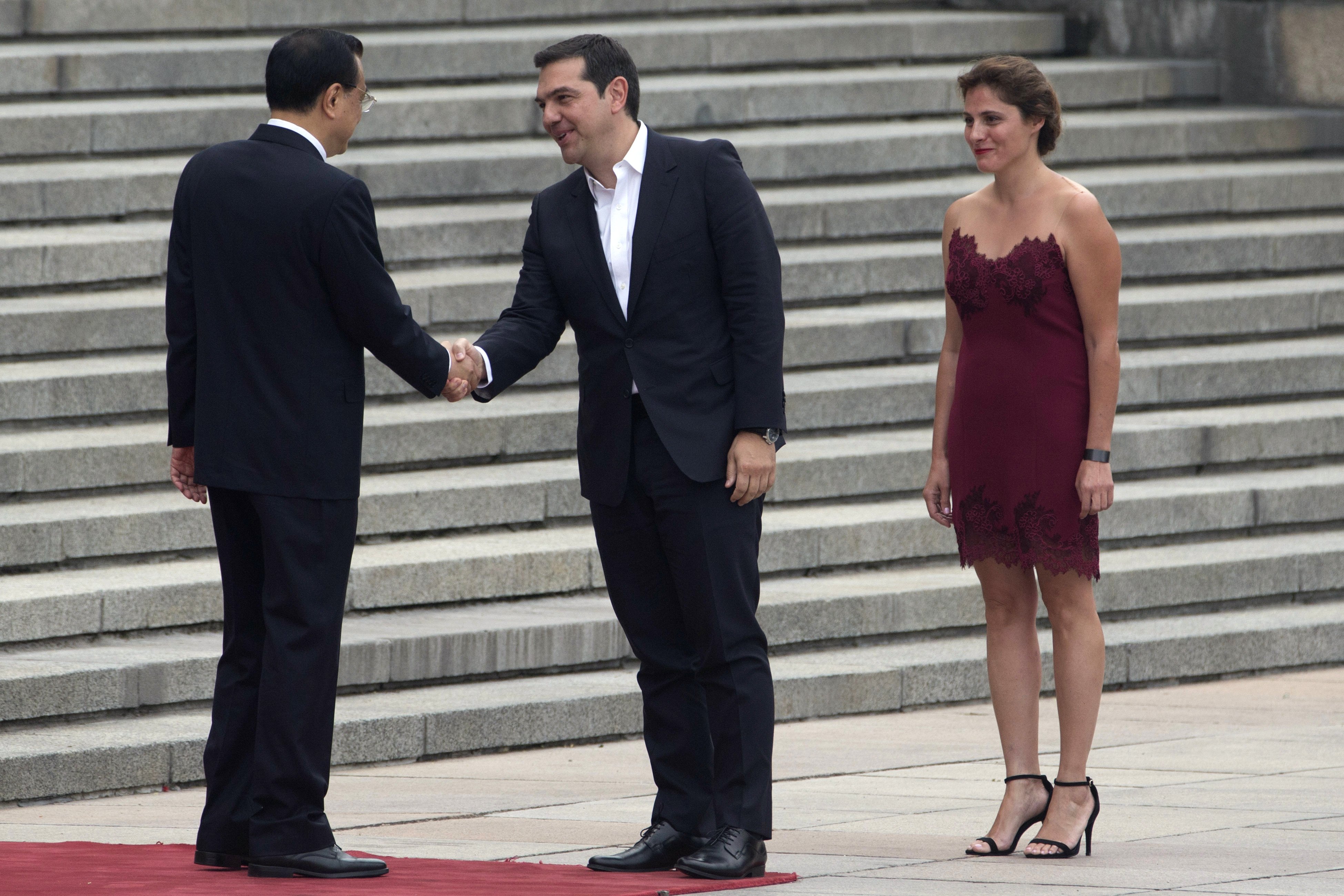 Greek Prime Minister Alexis Tsipras, center with his partner Peristera Baziana, right, is welcomed by Chinese Premier Li Keqiang at left during a welcome ceremony outside the Great Hall of the People in Beijing, China, Monday, July 4, 2016. (AP Photo/Ng Han Guan)